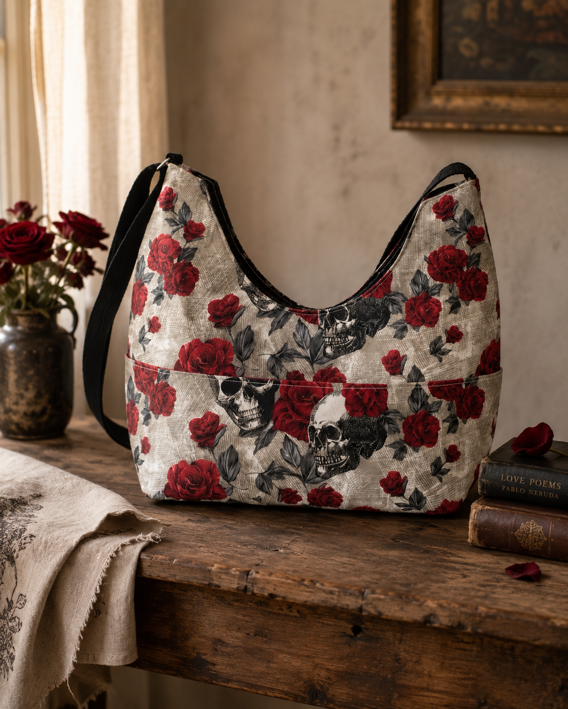 Floral and skull patterned bag on a wooden surface with books and flowers.