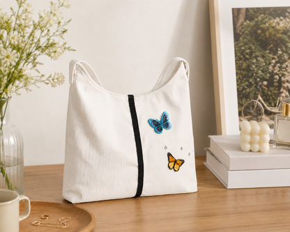White tote bag with butterfly designs on a wooden surface with decorative items.