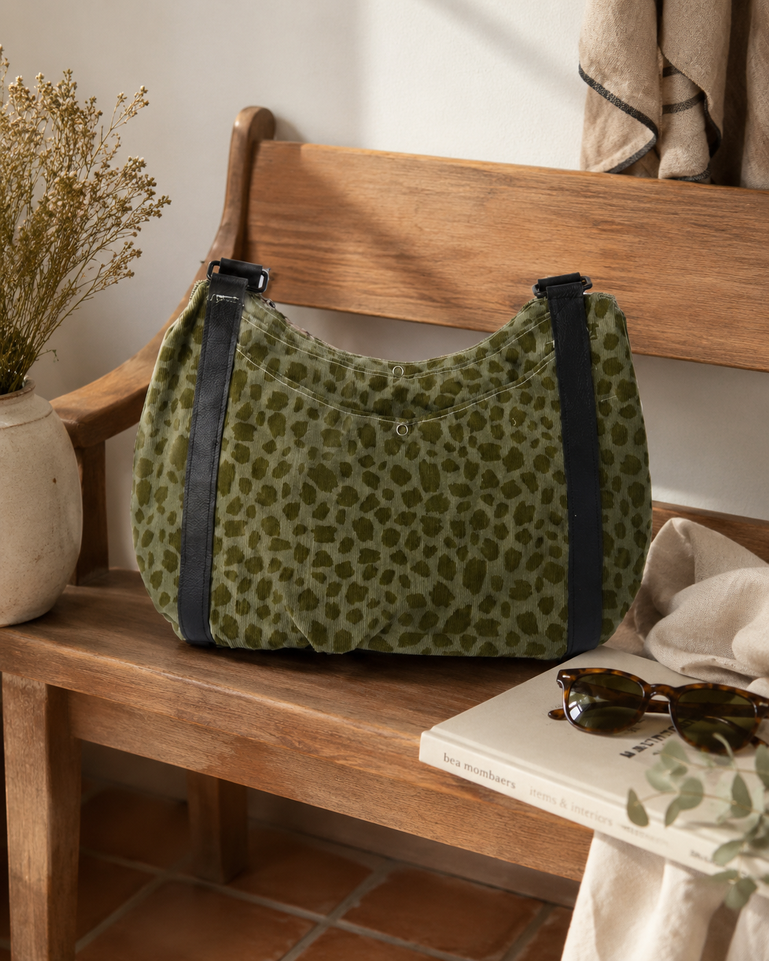 Green leopard print bag on a wooden bench with a plant and sunglasses in the background.