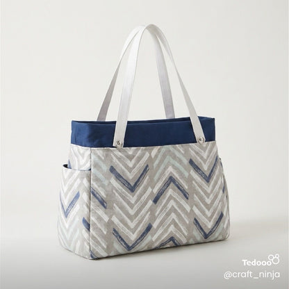 Tote bag with chevron pattern in navy blue, light gray and white, with  navy accents and white leather handles on a light gray background