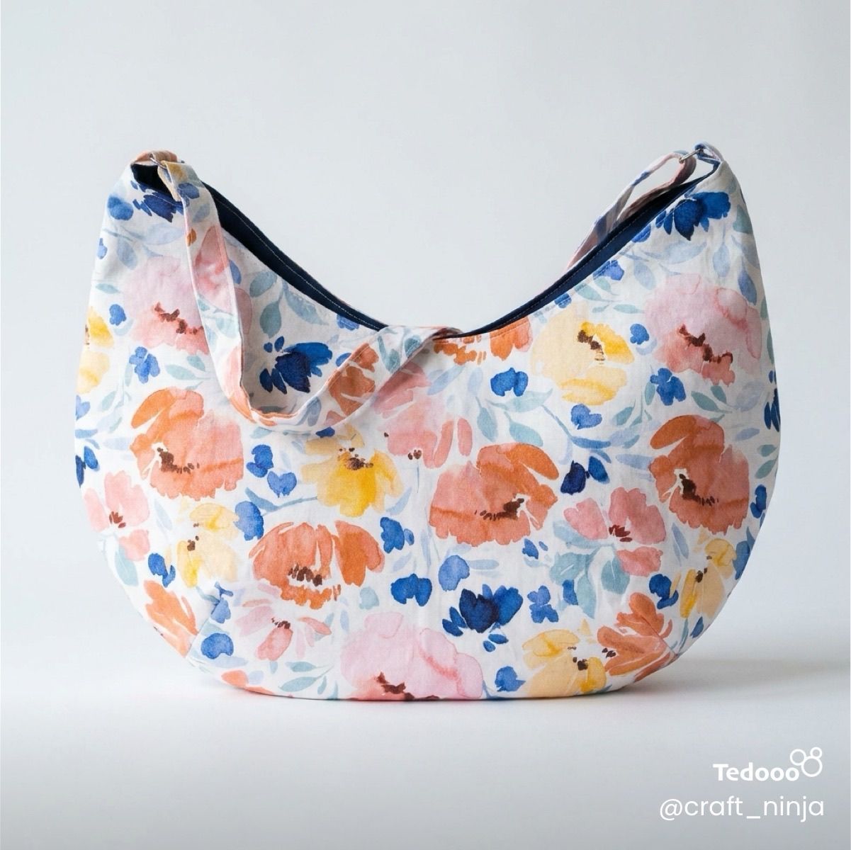 Floral patterned hobo style bag with yellow, orange and blue and a blue interioron a light gray background