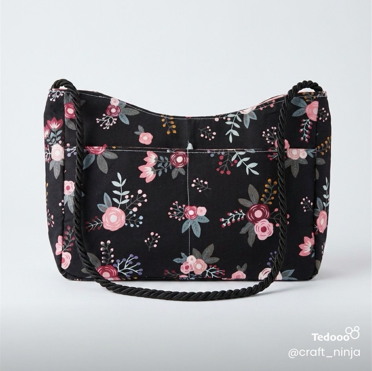 Light and dark pink floral-patterned handbag on a black background with a black rope handle.